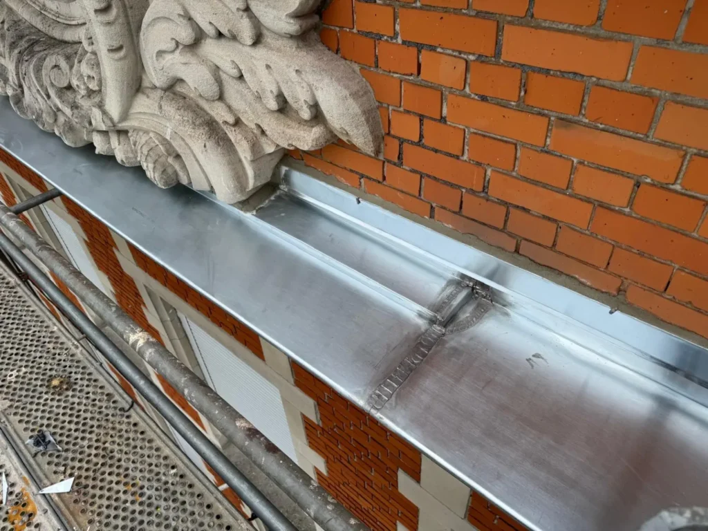 Détail du chéneau en zinc façonné autour des ornements de façade